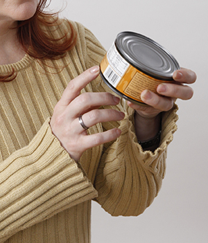 Closeup of woman's hands holding can of food, pointing at nutrition label.