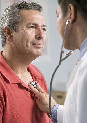 Doctor listening to man's chest with stethoscope.